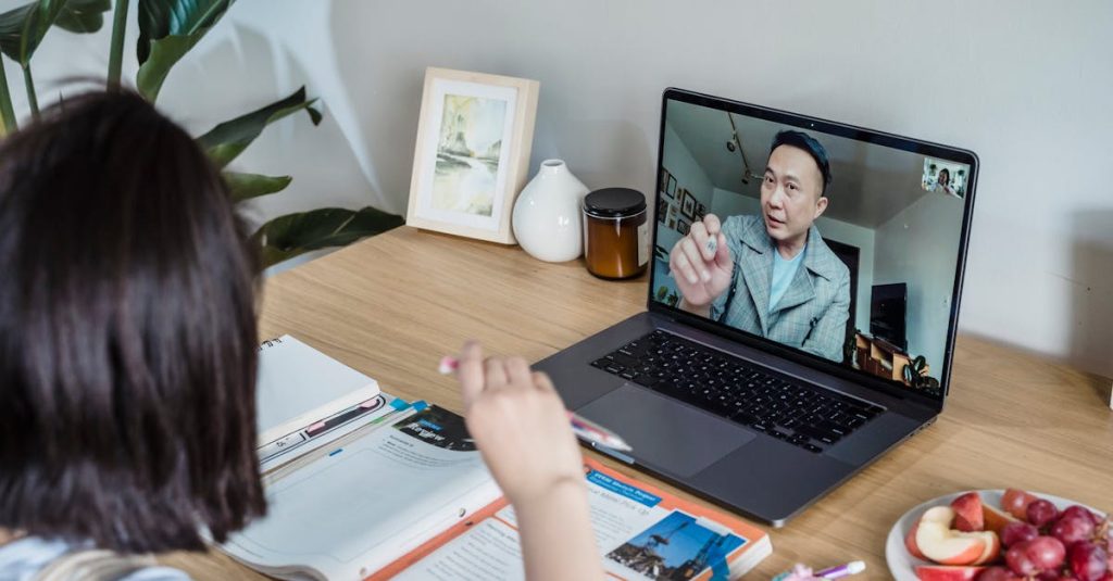 A young woman engaged in an online learning session via laptop surrounded by study materials and snacks on a wooden table.