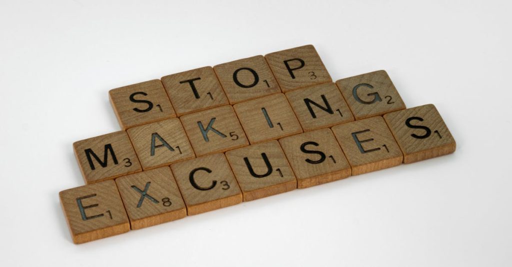 Wooden Scrabble tiles spell 'Stop making excuses' on a white background, encouraging self-improvement.